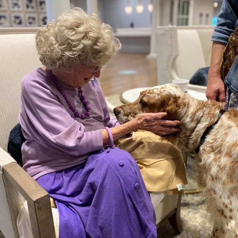 Lady at Assisted Living petting a dog while sitting in chair.